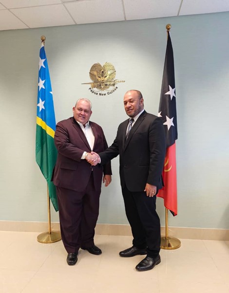 HC William Soaki and DG Loenard Louma standing in front of the MSG and Solomon Islands flags at the Solomon Islands High Commission.